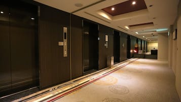 Un pasillo de hotel con puertas de madera oscura, alfombra estampada e iluminación empotrada en el techo.