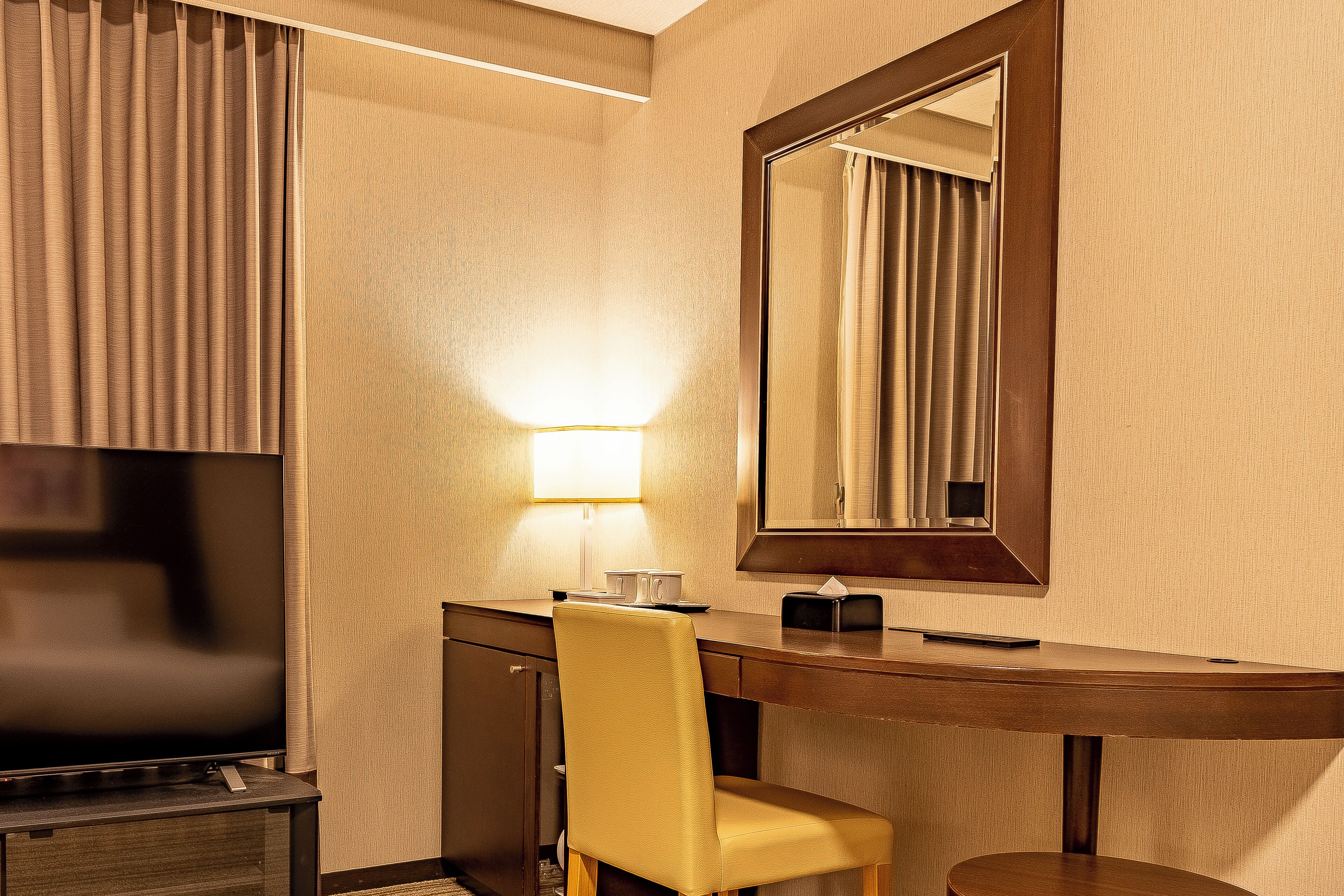 Une chambre d’hôtel équipée d’une télévision à écran plat, d’un bureau avec une lampe, d’une chaise et d’un miroir.