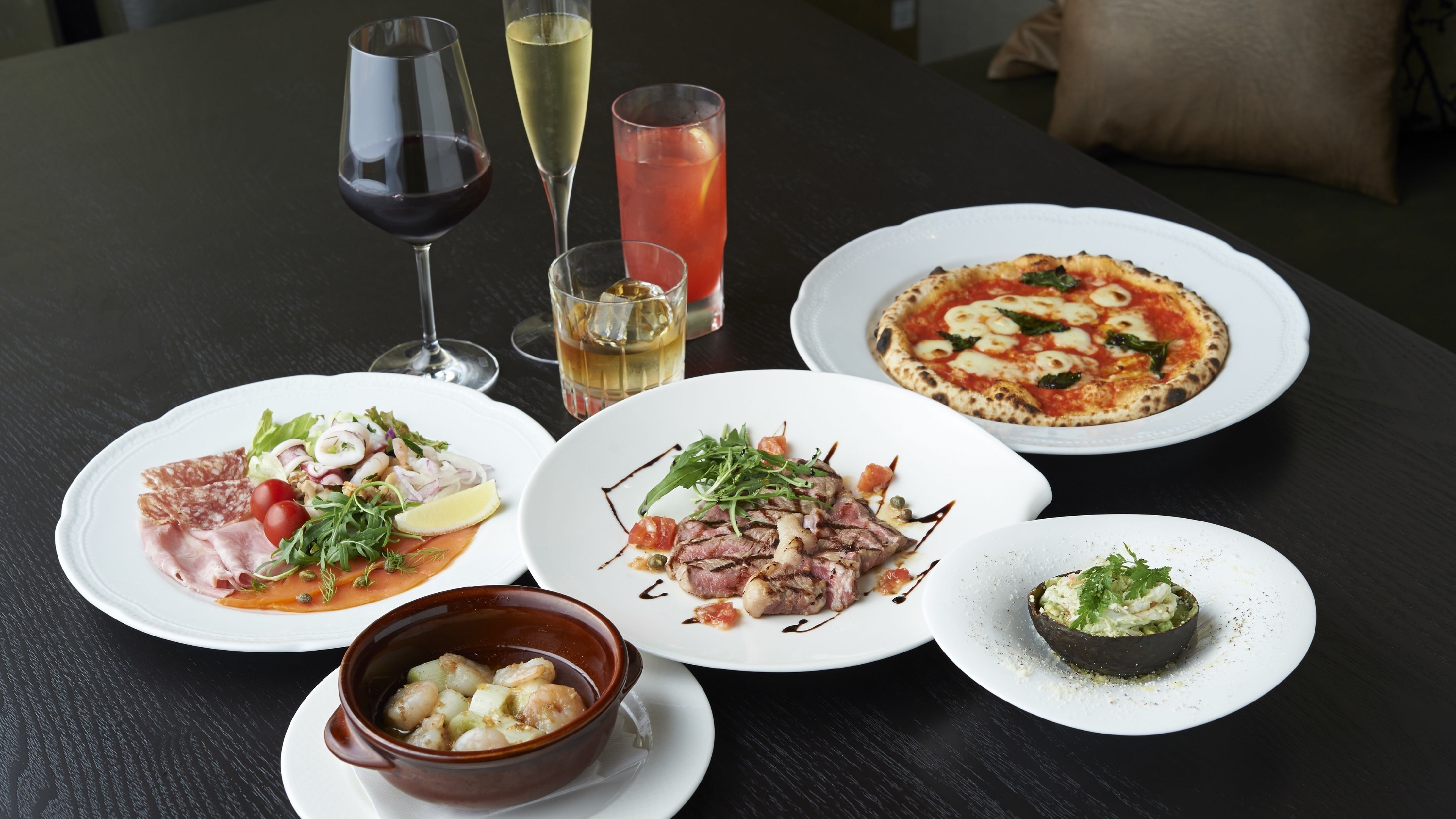 A table set with various dishes, including a pizza, a bowl of soup, and plates with meat and vegetables.