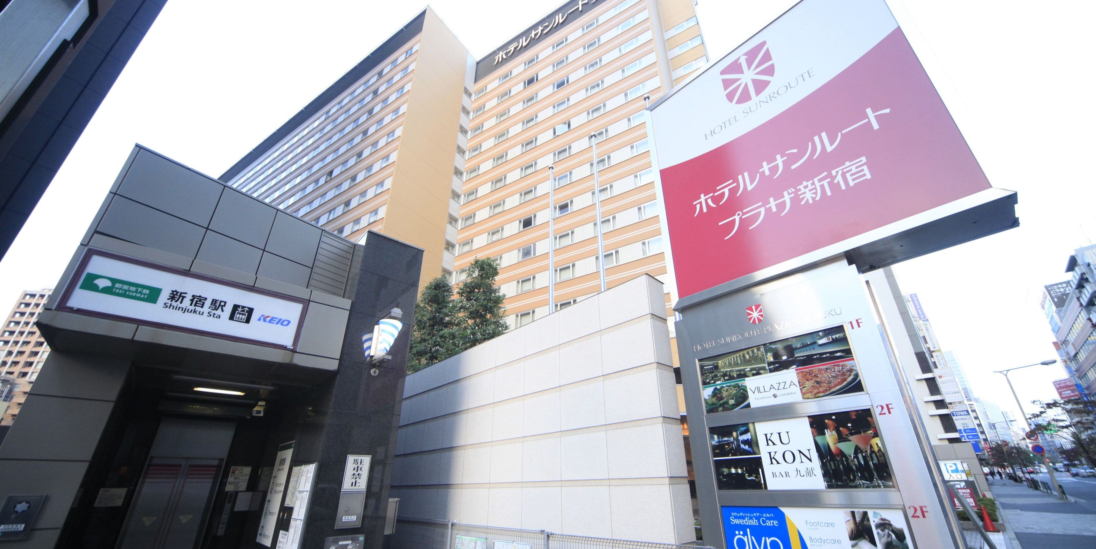 Um hotel com vários andares, um letreiro bem visível do Hotel Sunroute e uma entrada com a indicação da Estação Shinjuku.