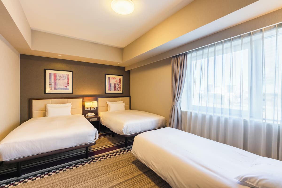 Une chambre d’hôtel avec deux lits, un comptoir d’enregistrement et une grande fenêtre avec des rideaux.