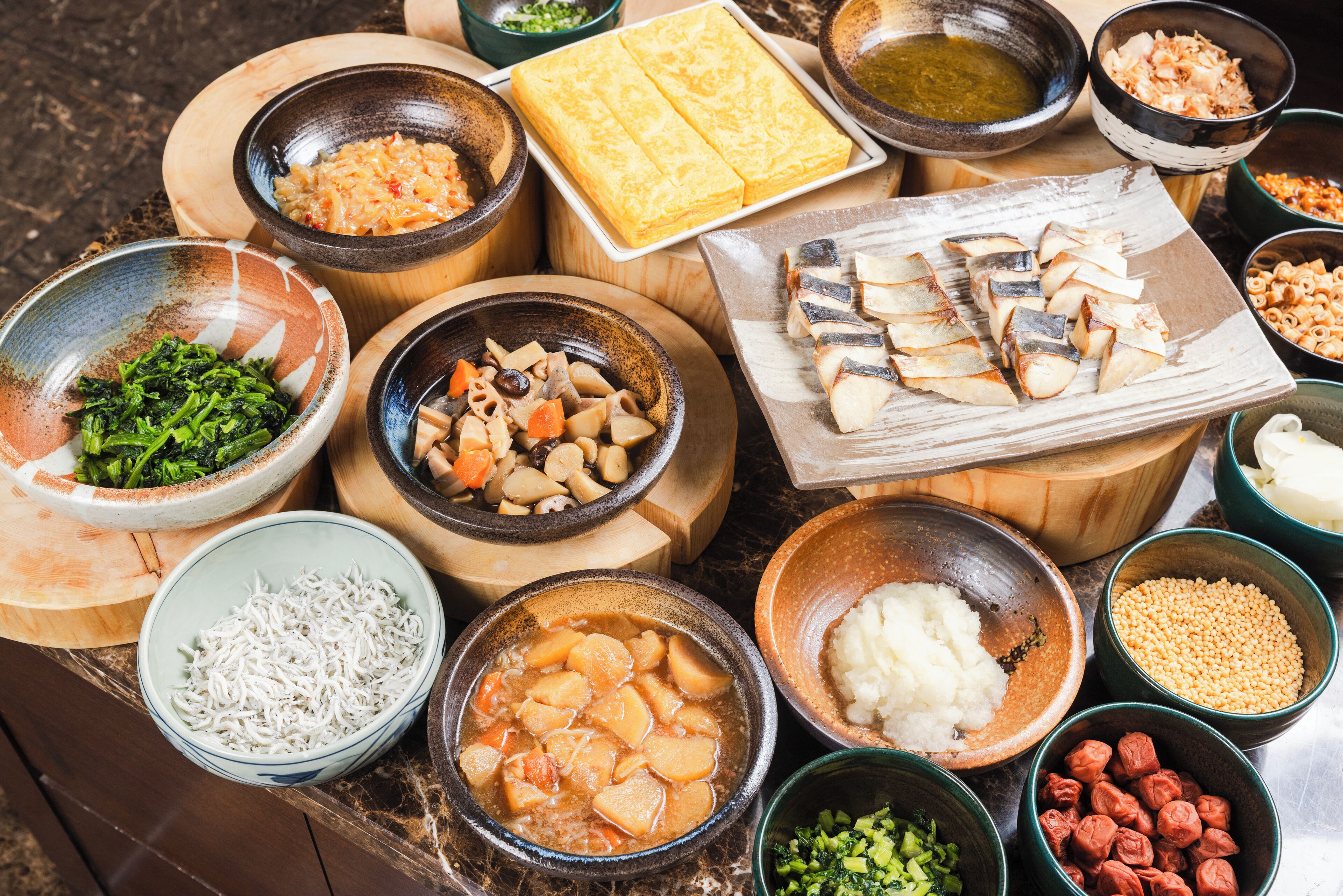 A variety of dishes including fish, vegetables, and noodles arranged on wooden tables.
