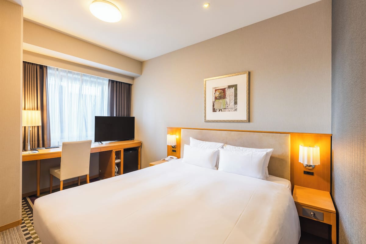 Une chambre d’hôtel avec un grand lit, un bureau avec un ordinateur, une télévision et un tableau accroché au mur.