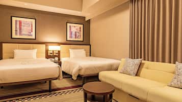 A hotel room with two beds, a sofa, a small table, and two framed artworks on the wall.