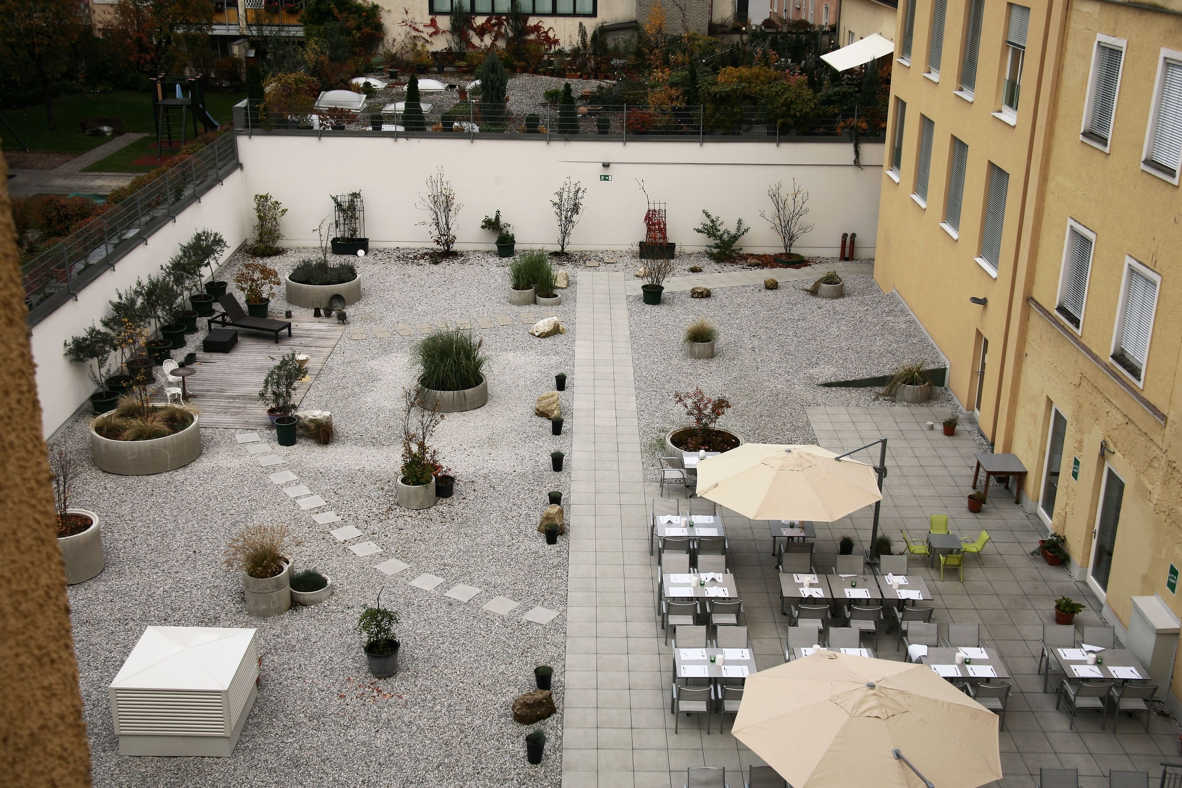Une cour avec des espaces de repos en plein air, des plantes en pot et un chemin.