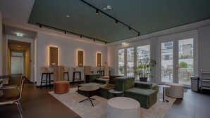 Um hall moderno com áreas de estar, balcão de recepção e grandes janelas com vista para a cidade.