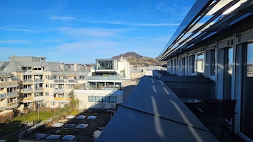 Un edificio moderno con varios balcones y amplias ventanas, con vistas a una zona residencial y una montaña.