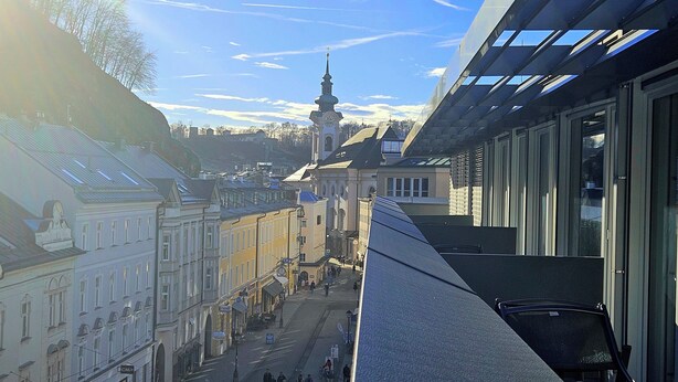 Vista de uma rua com edifícios históricos, uma torre de igreja e um edifício moderno com grandes janelas.