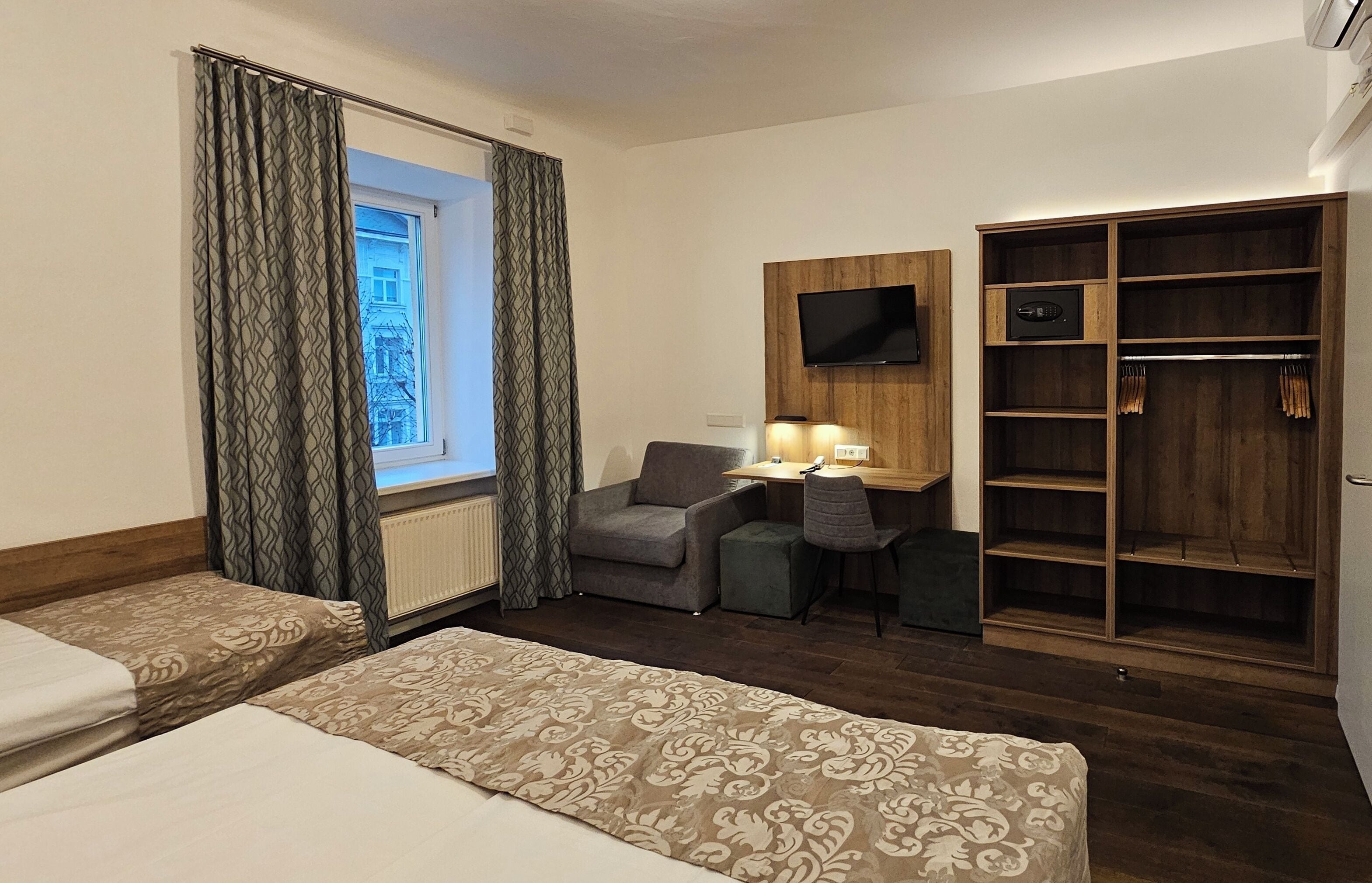 A hotel room with two beds, a desk with a lamp, a TV, and a wardrobe.