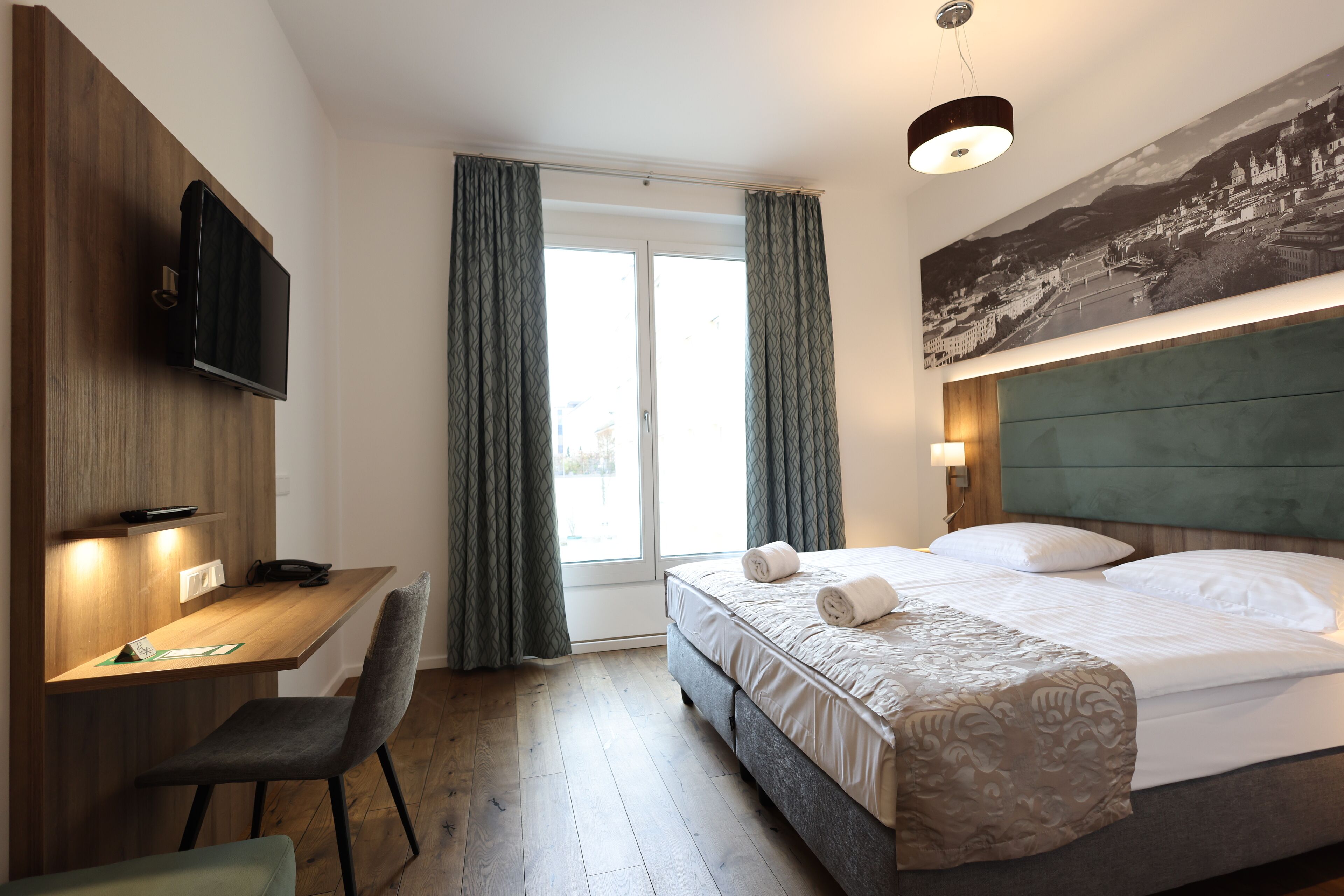 Une chambre d’hôtel équipée d’un lit, d’un bureau, d’une chaise, d’une télévision et d’une grande fenêtre avec des rideaux.