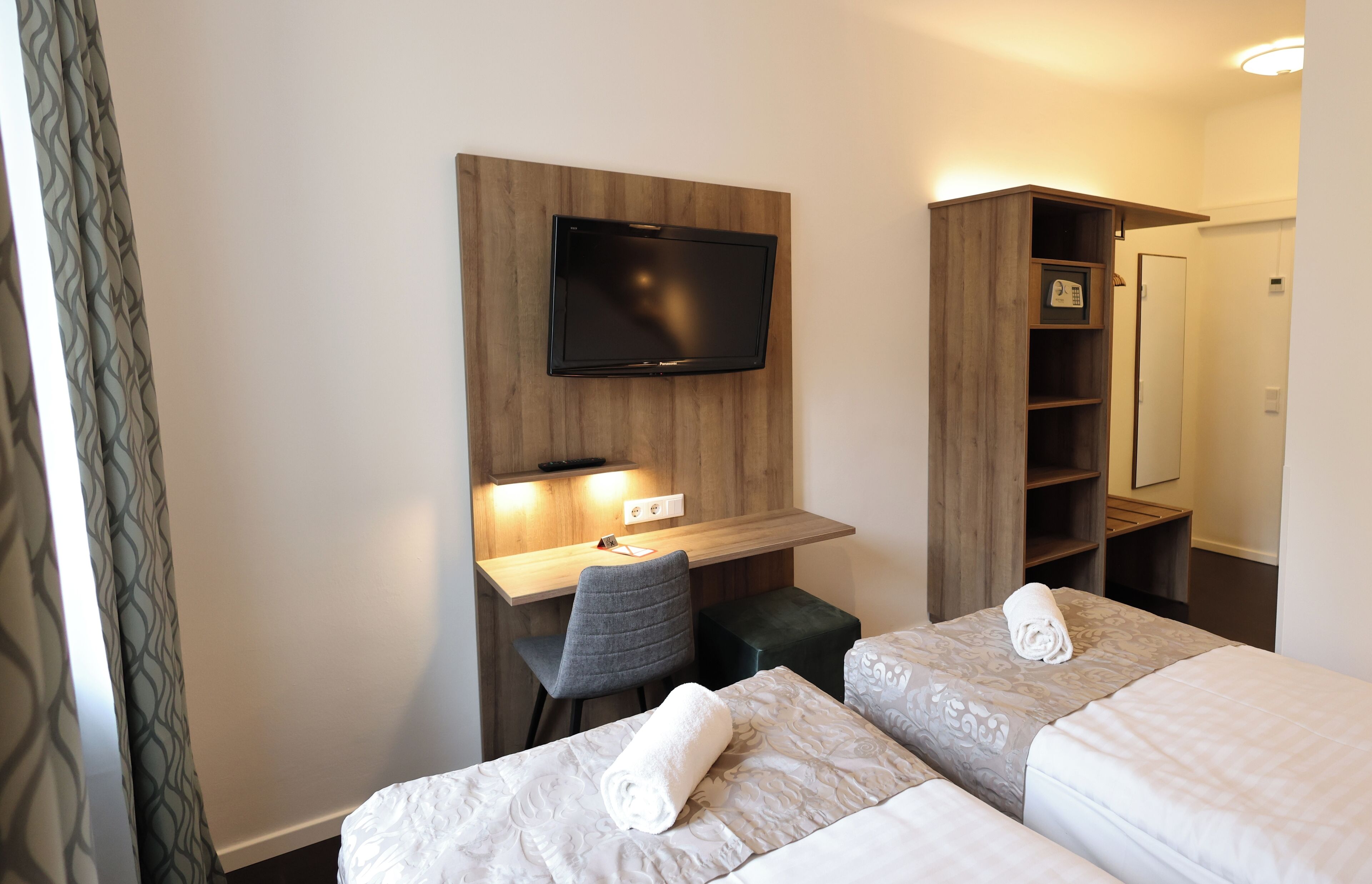 A hotel room with two beds, a desk with a chair, a television mounted on the wall, and a wardrobe.