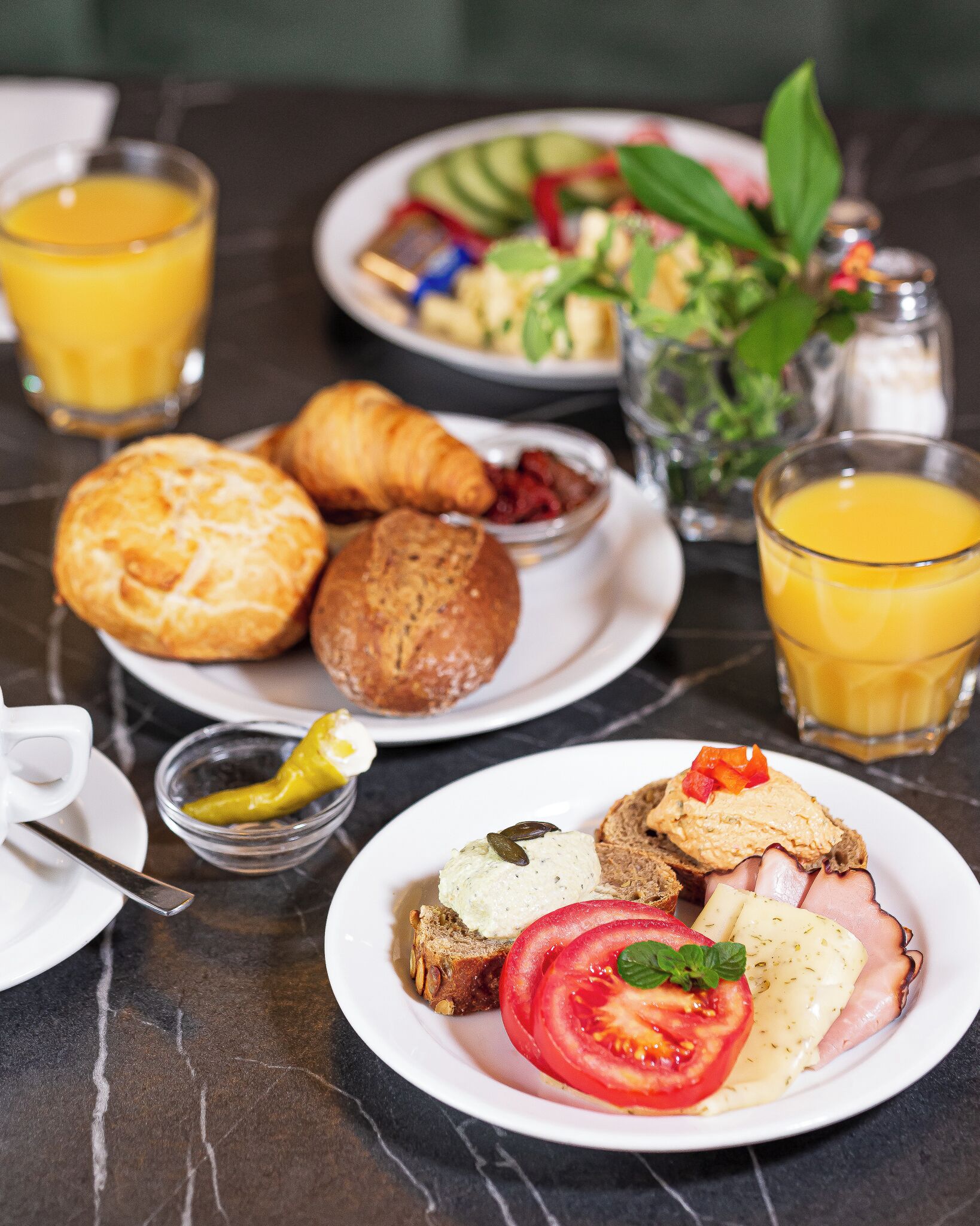 A breakfast setting with croissants, a plate of eggs, tomatoes, and a glass of orange juice.