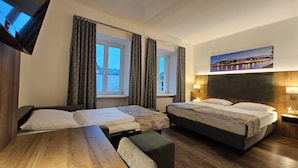 A hotel room with two beds, a wooden table, a bench, and a painting of a cityscape.