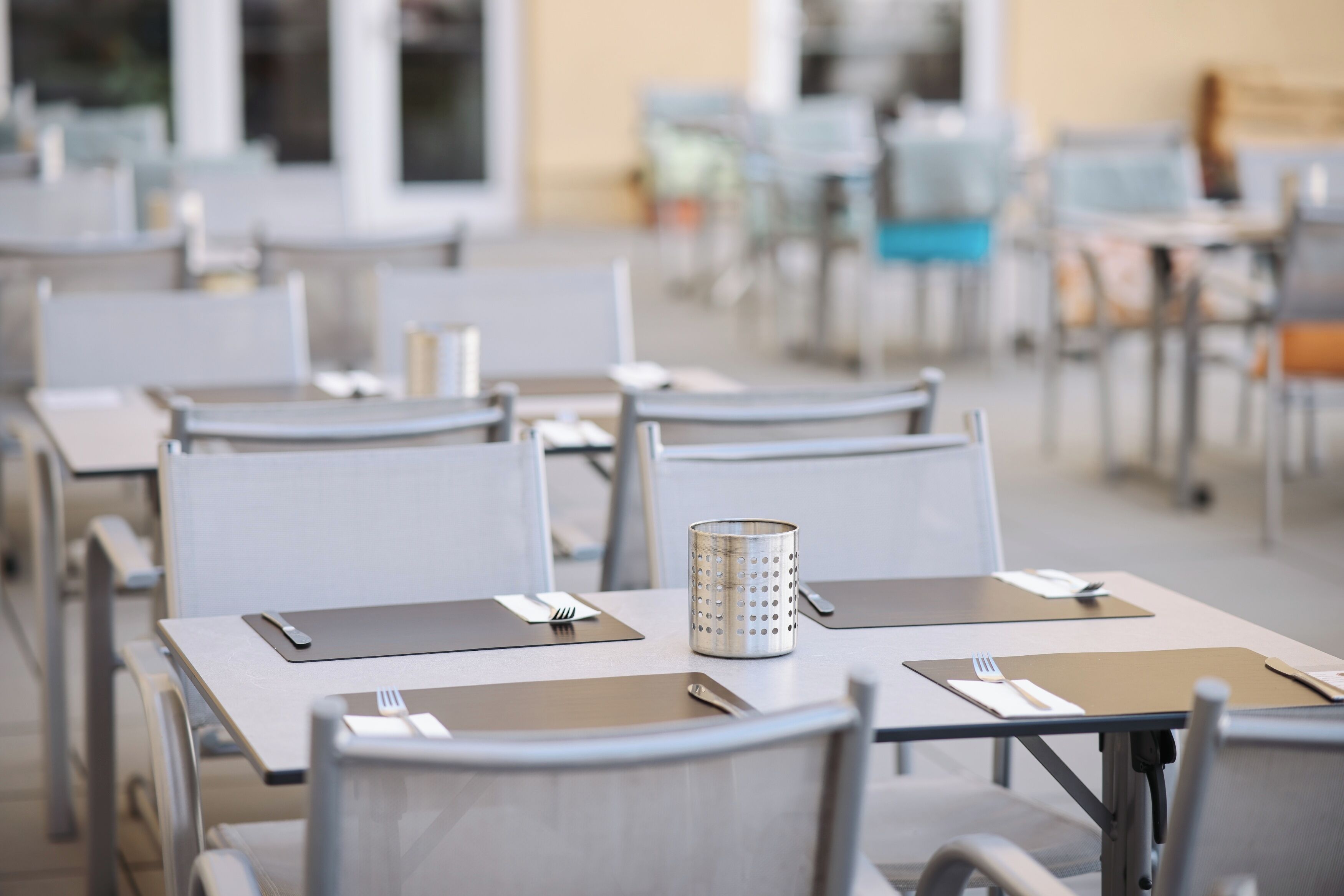 Un comedor con mesas dispuestas para dos, cada una con un mantel individual, cubiertos y un candelabro.