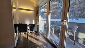 A balcony with a table and chairs, a sliding glass door, and a view of a hillside.