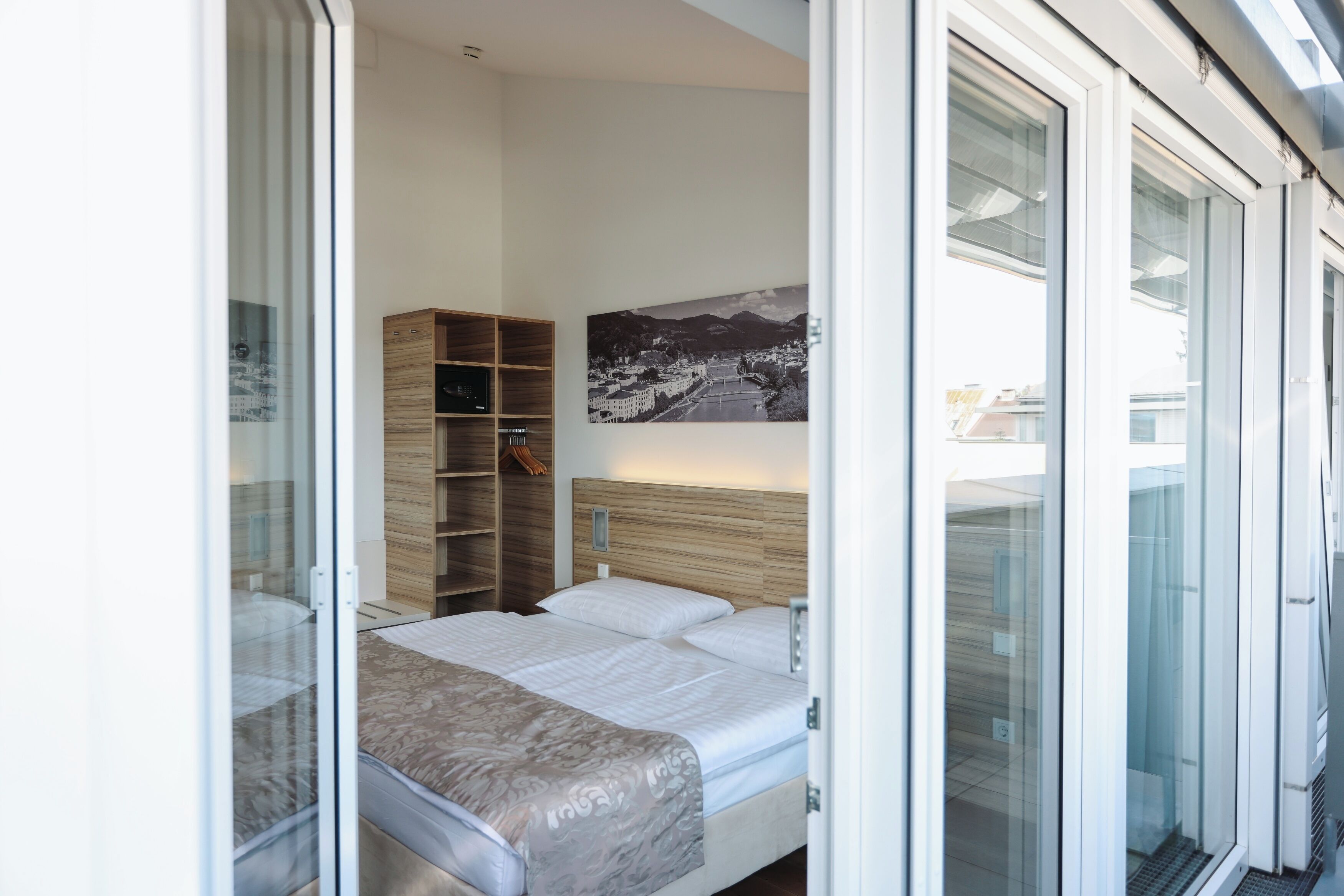Ein modernes Schlafzimmer mit einem Bett, einem Holzschrank und einem großen Fenster mit Blick auf die Stadt.