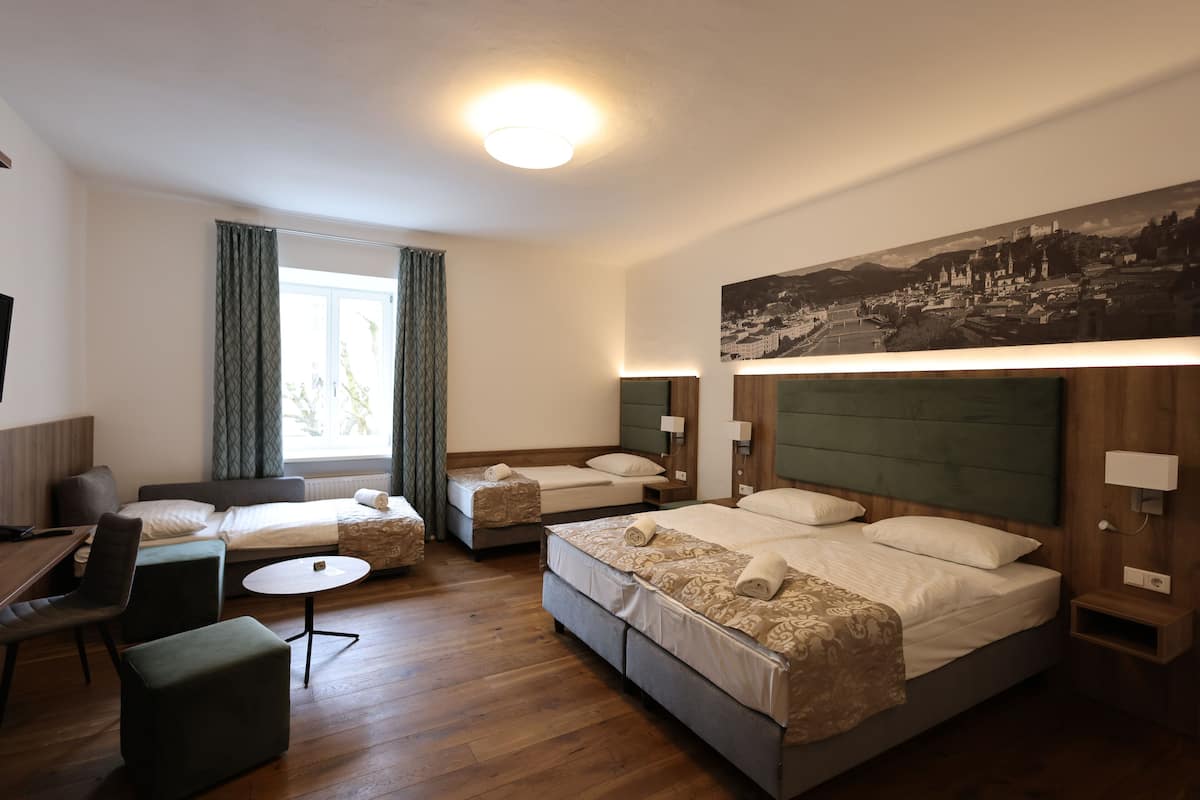 A hotel room with two single beds, a sofa bed, a small table, and a TV.