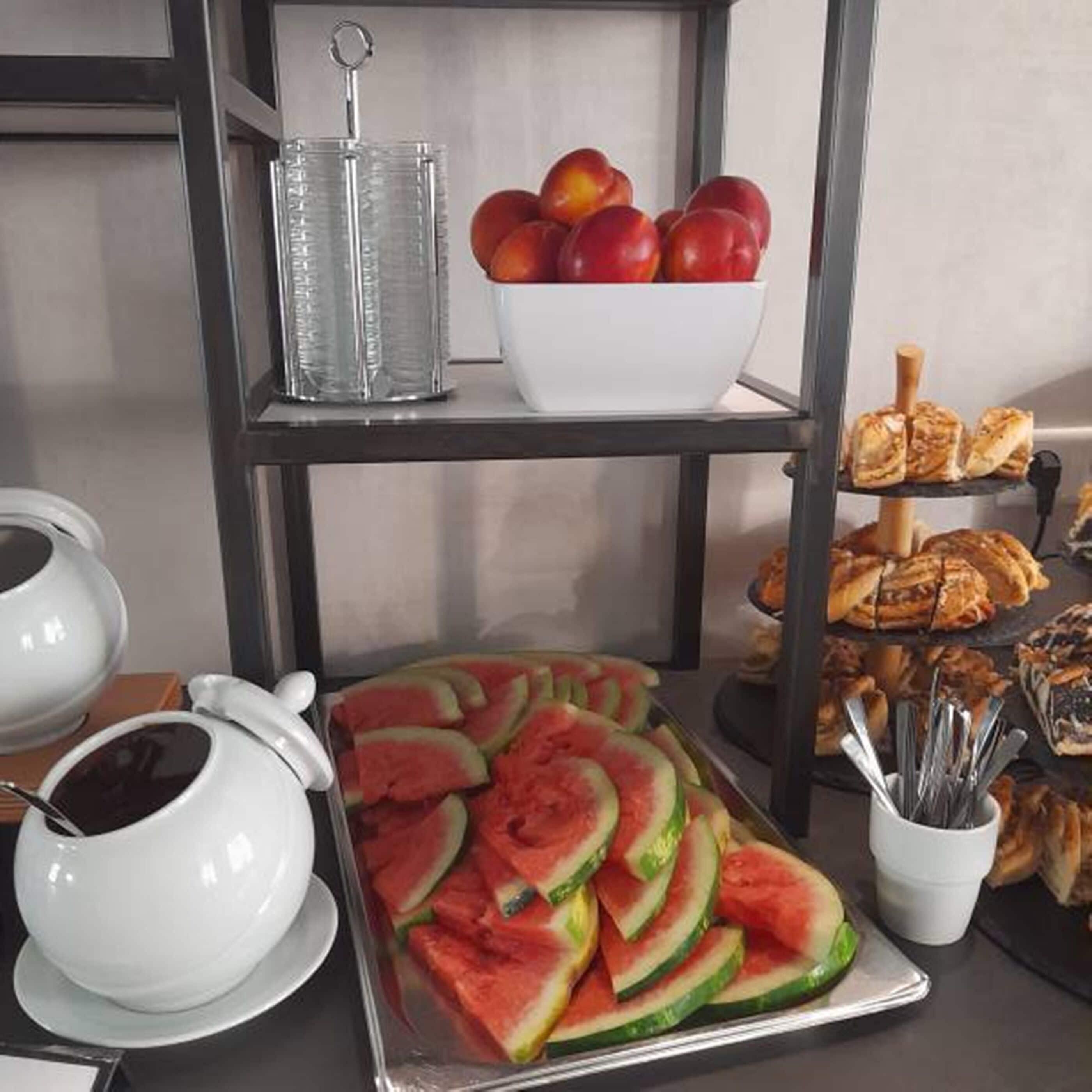 A breakfast buffet with sliced watermelon, a bowl of fruit, and pastries.