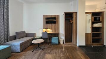 A modern living room with a sofa, a small round table, a chair, and a wooden desk with a TV mounted above it.