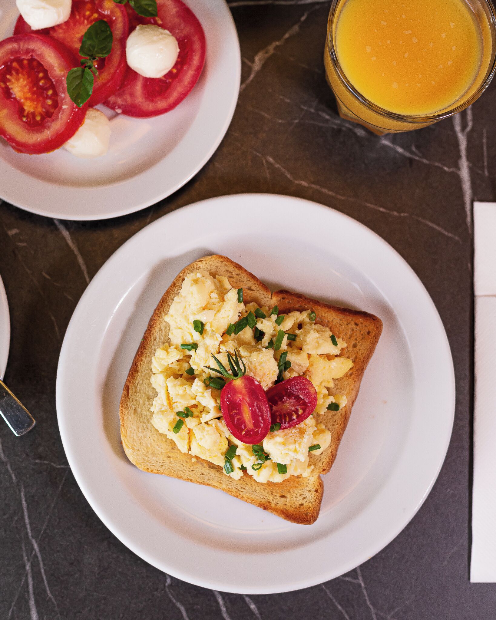 A breakfast plate with scrambled eggs, cherry tomatoes, and a glass of orange juice.