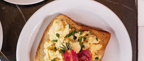 A breakfast plate with scrambled eggs, cherry tomatoes, and a glass of orange juice.