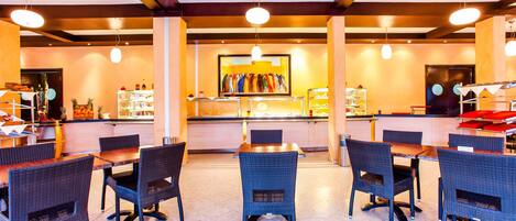 Un restaurante con mesas altas y sillas de mimbre, una barra con exhibición de bebidas y un cuadro grande en la pared.