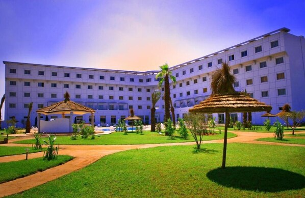 Un gran hotel con varios pisos, un patio central con palmeras y una piscina.