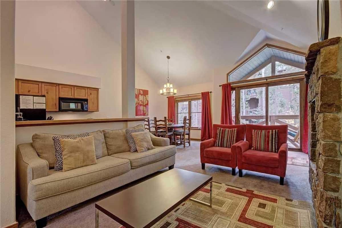 A living room with a sofa, a red sofa, a coffee table, and a dining area with a table and chairs.