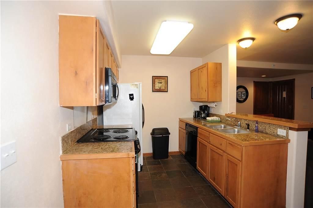 A compact kitchen with wooden cabinets, a stove, a refrigerator, a dishwasher, and a granite countertop.