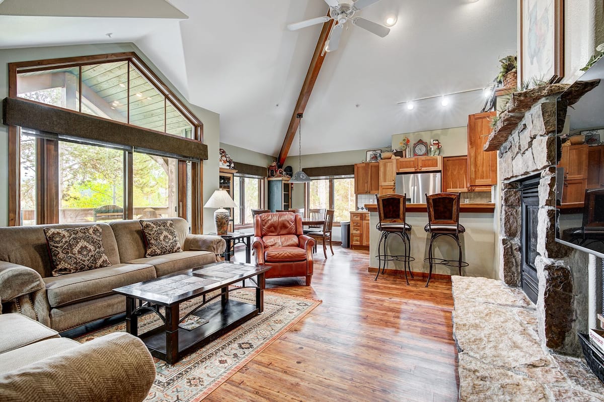 A spacious living room with a high ceiling, a fireplace, and a view of the outdoors.