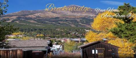A mountain view with a town in the foreground, a wooden cabin, and a sign that reads "Brecknridge, Your Home Away From It All".