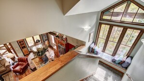 Un loft espacioso con techo alto, una mesa de comedor de madera, una zona de cocina y un amplio asiento junto a la ventana con vistas a un jardín.