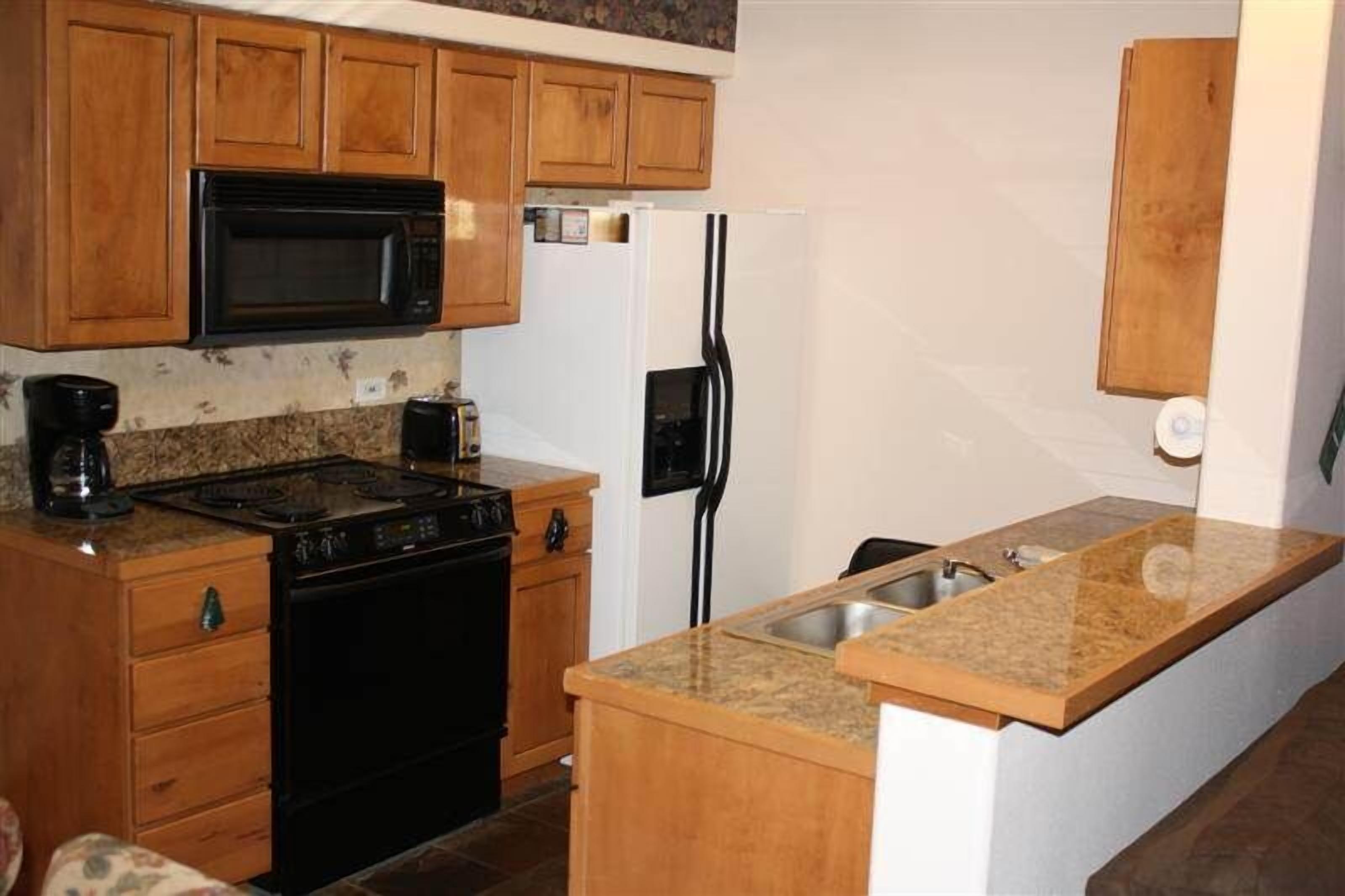 A compact kitchen with wooden cabinets, a black microwave, a white refrigerator, and a granite countertop.