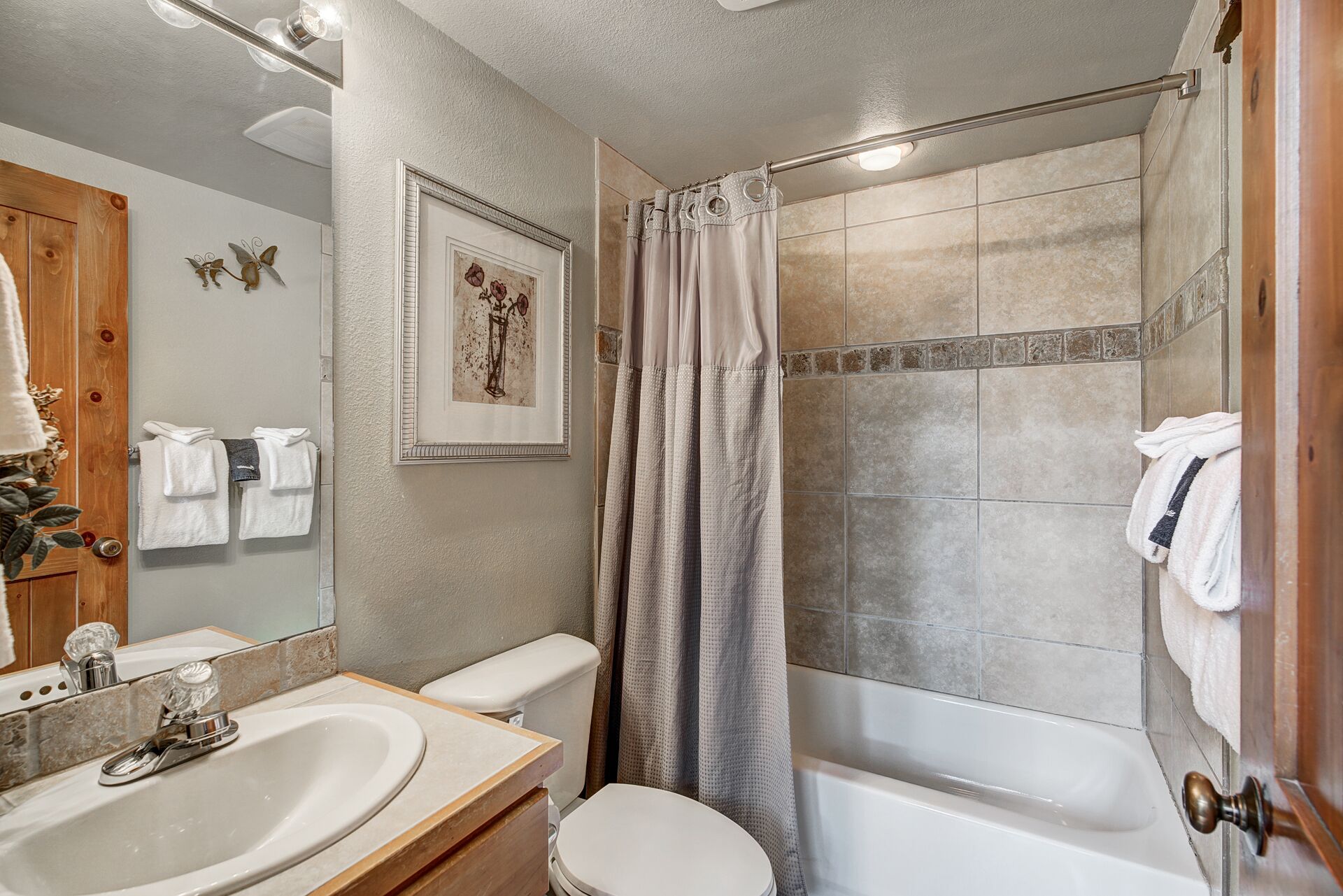 A bathroom with a sink, toilet, and bathtub. There is a shower curtain and towels on the wall.