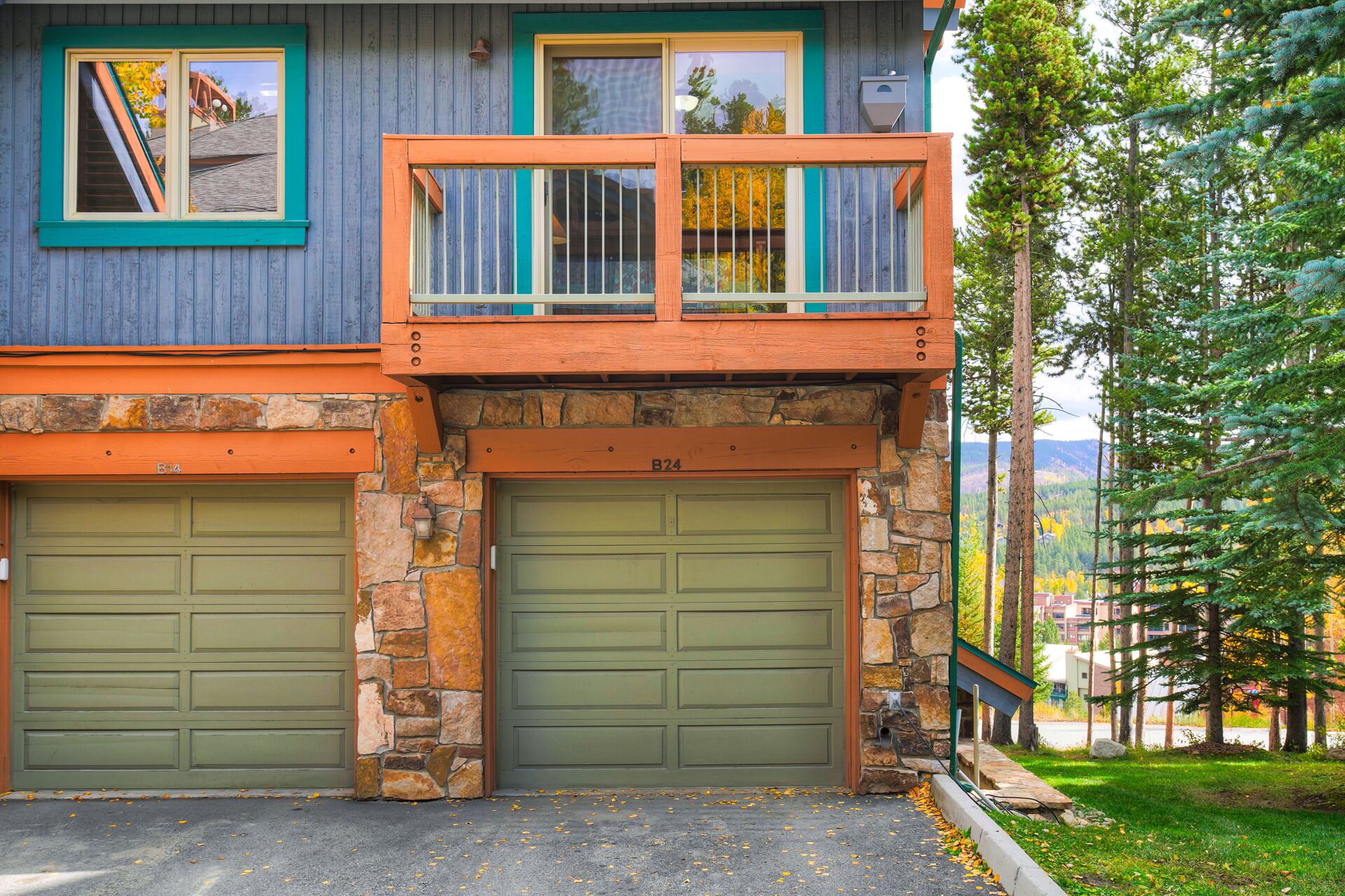Een huis met twee verdiepingen, een stenen gevel, een balkon met een hekwerk en twee garagepoorten.
