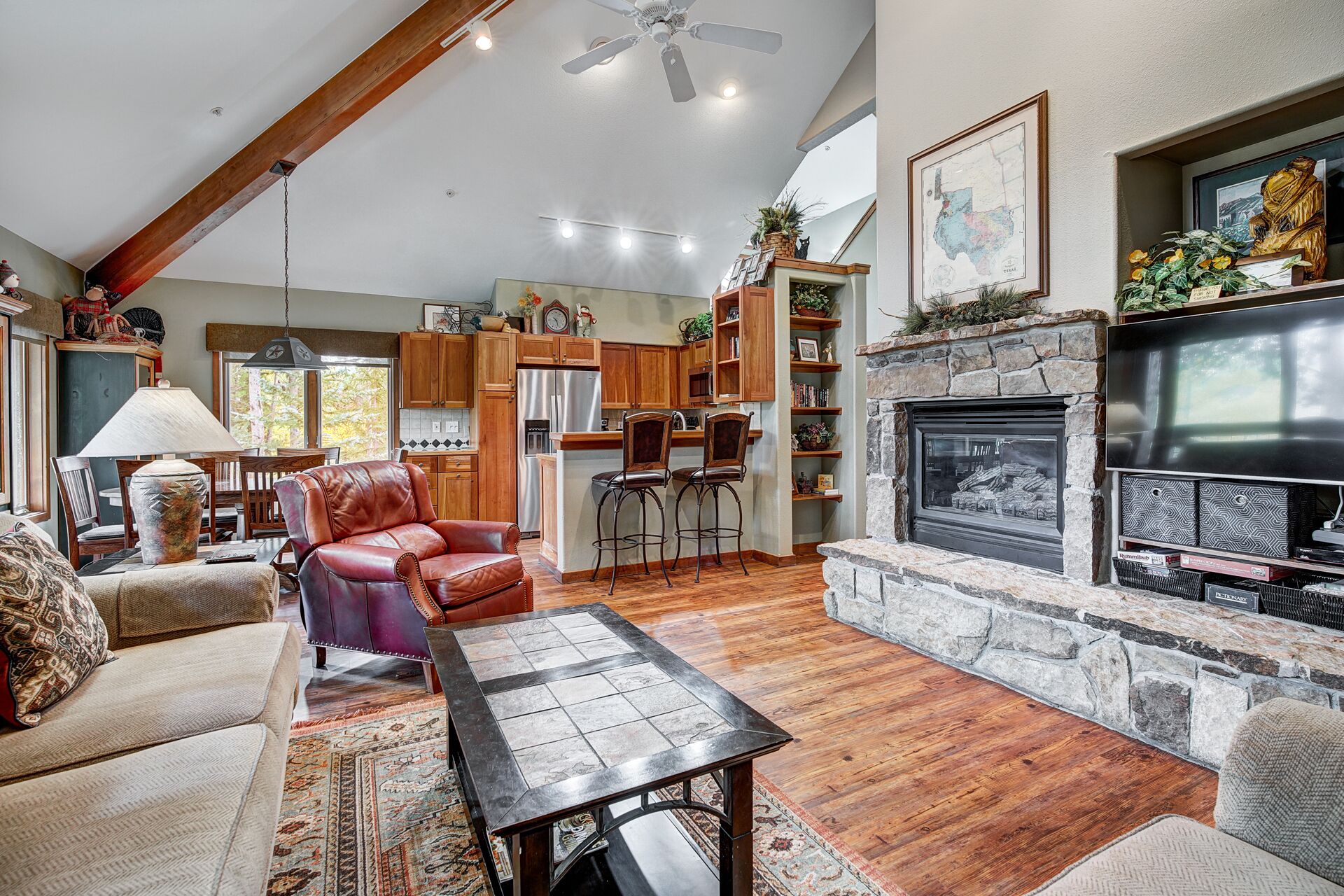 A spacious living room with a fireplace, wooden beams, and a stone fireplace surround.