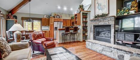A spacious living room with a fireplace, wooden beams, and a stone fireplace surround.