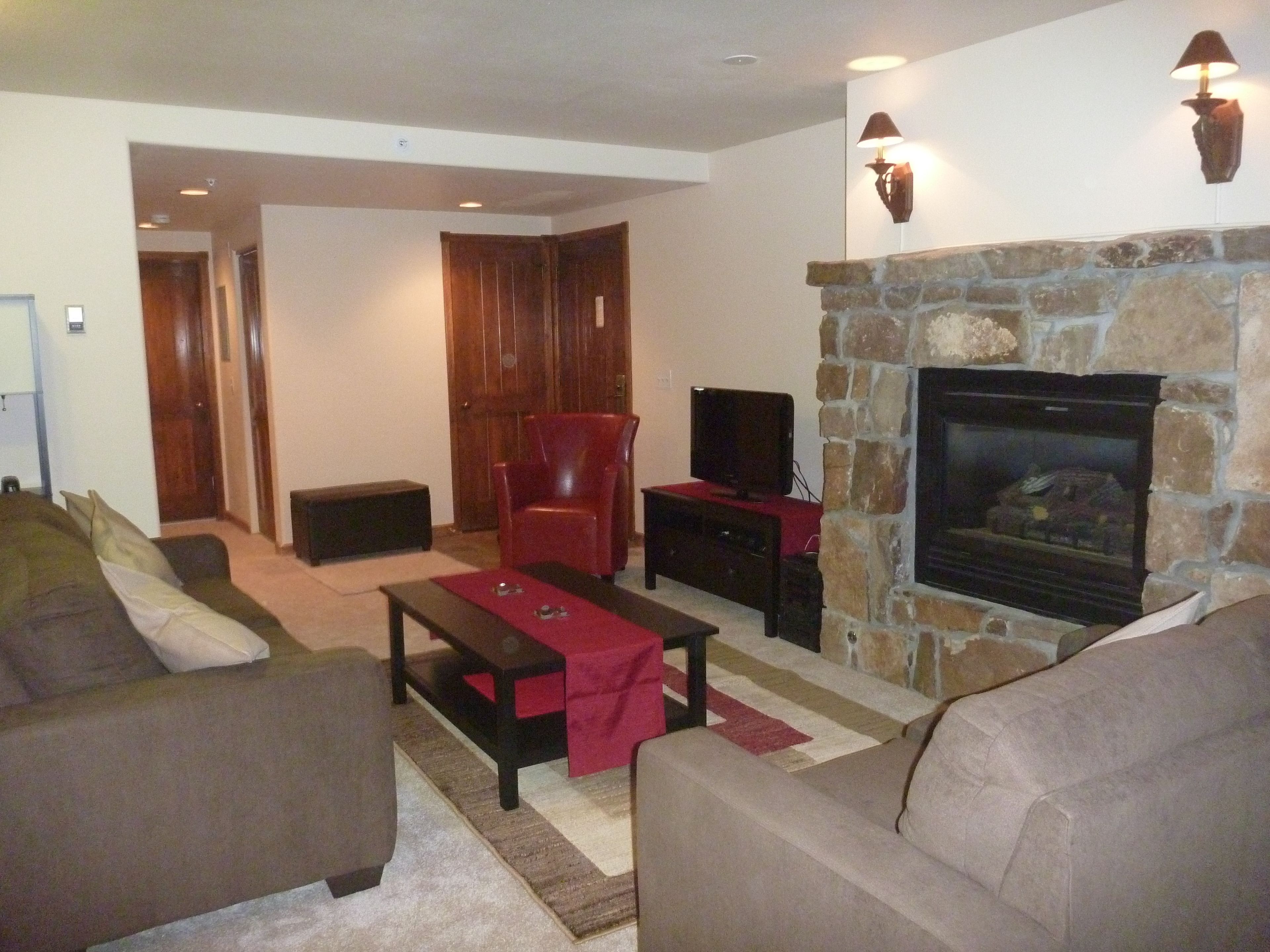 A living room with a stone fireplace, leather armchair, and a television on a stand.