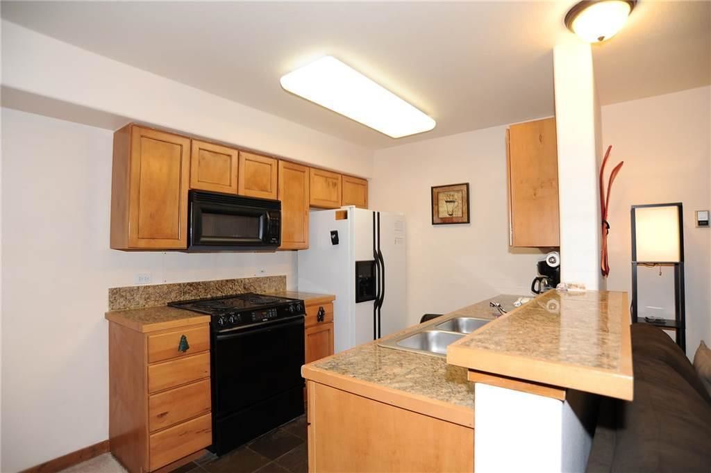 A kitchen with wooden cabinets, a black stove, a white refrigerator, granite countertops, and a built-in sink.