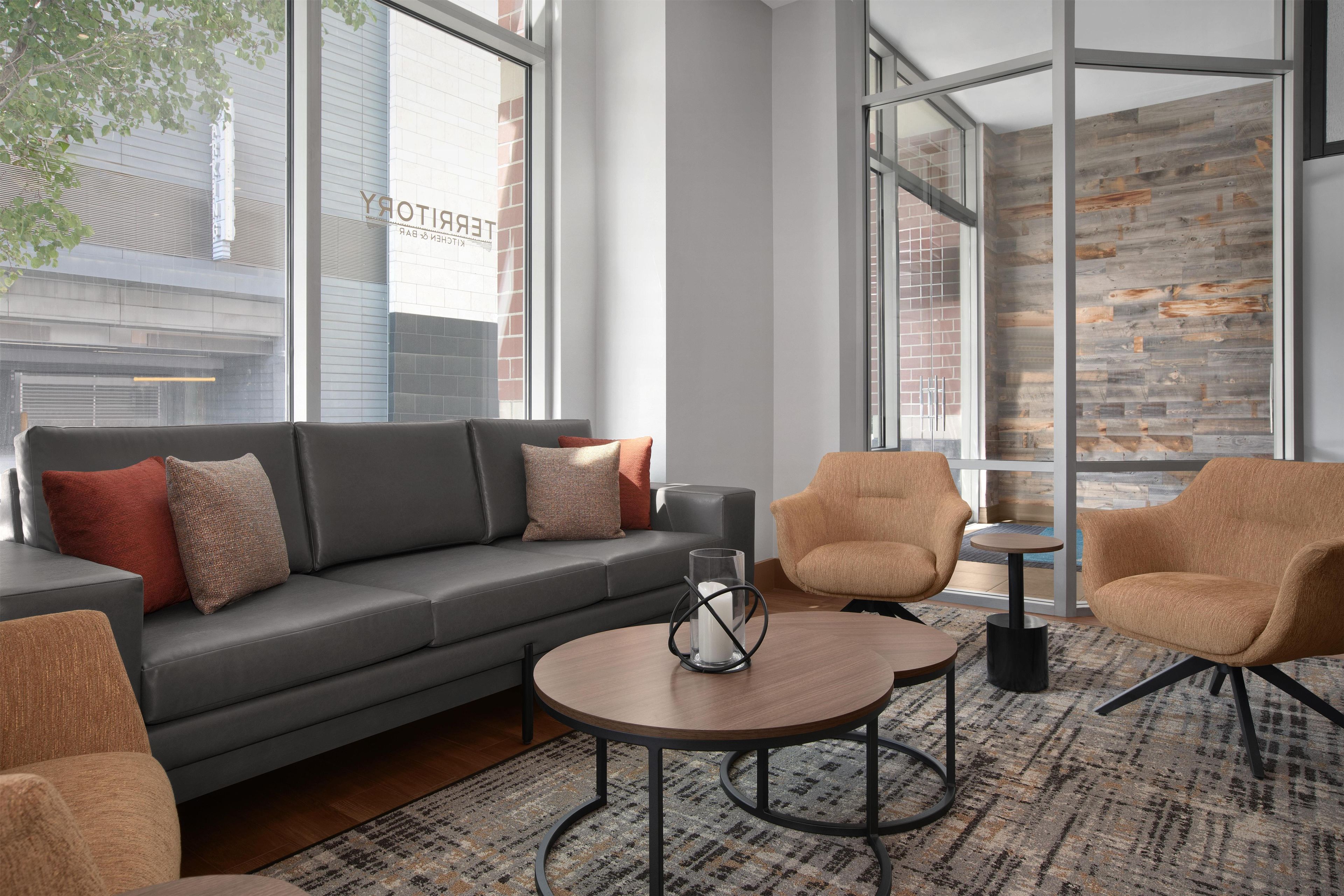 A modern lounge area with a grey sofa, two armchairs, a coffee table, and a patterned rug.