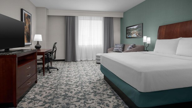 A hotel room with a bed, a desk with a lamp, a chair, and a television. - Hilton Garden Inn Denver Downtown (Denver)
