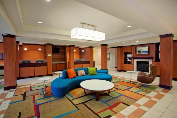 A spacious lobby with a blue sofa, a round coffee table, and a fireplace. - Fairfield Inn & Suites by Marriott Detroit Metro Airport Romulus (Romulus)