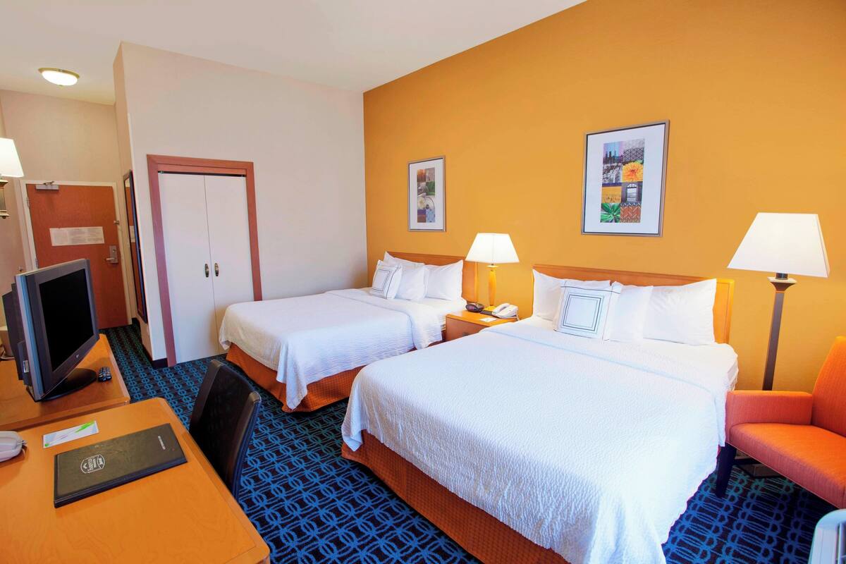 Une chambre d’hôtel avec deux lits, un bureau avec un ordinateur, une chaise et un téléviseur.