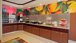 Cocina de hotel con barra tipo bufé, que incluye un refrigerador, estación de alimentos calientes y diferentes opciones de comida a la vista.