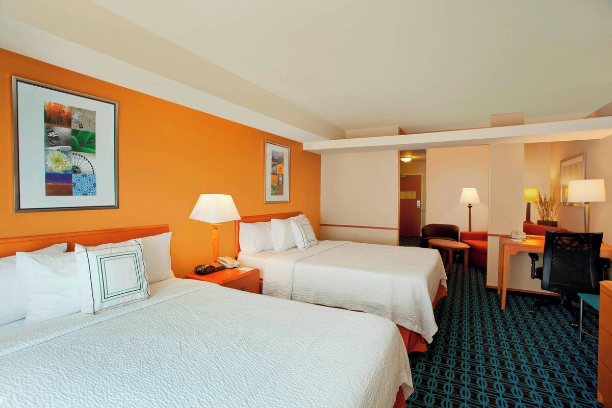 Une chambre d’hôtel avec deux lits, un bureau, une chaise et une petite table.
