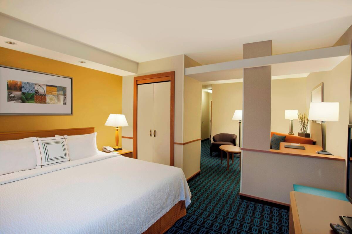 Une chambre d’hôtel avec un lit, un bureau, une chaise, une lampe et un tableau encadré au mur.
