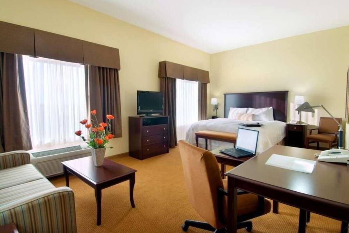 A hotel room with a bed, a desk with a laptop, a TV, a dresser, and a chair.