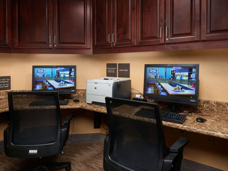 A hotel reception area with two computer monitors, a printer, and two office chairs.