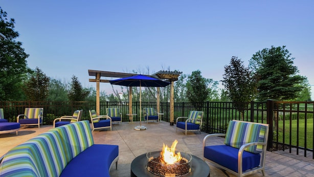 An outdoor patio with a fire pit, lounge chairs, and a pergola with a blue umbrella. - Hampton Inn & Suites Rogers (Rogers)