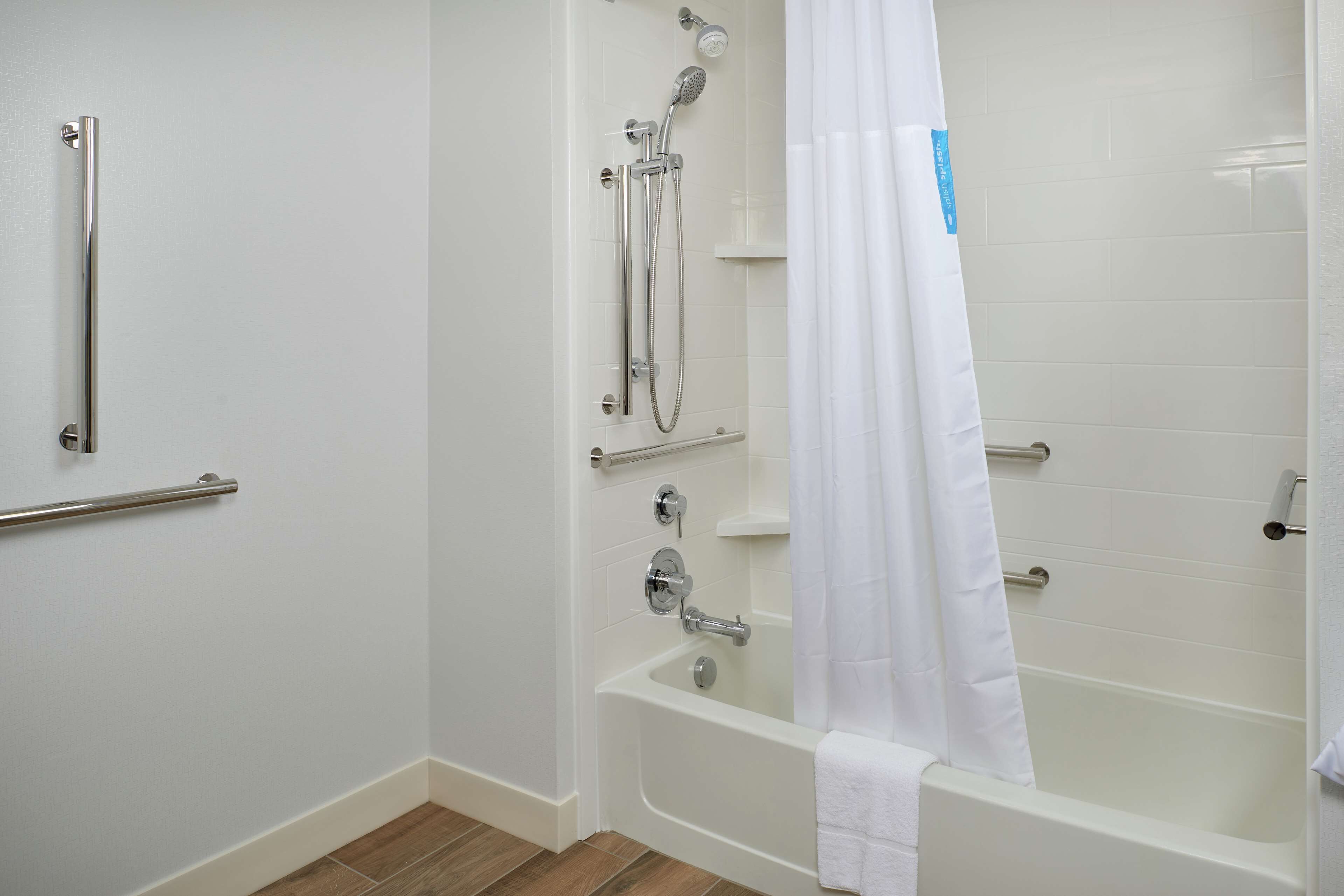 A bathroom with a bathtub, a shower, and a handrail.